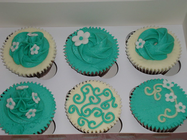 A gift box of chocolate cupcakes with teal and cream buttercream icing and