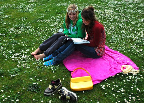 On a pink, green, and white cloud, two young women reading a book at Greenlake, with a daisy chain in a field of flowers, Seattle, Washington, USA