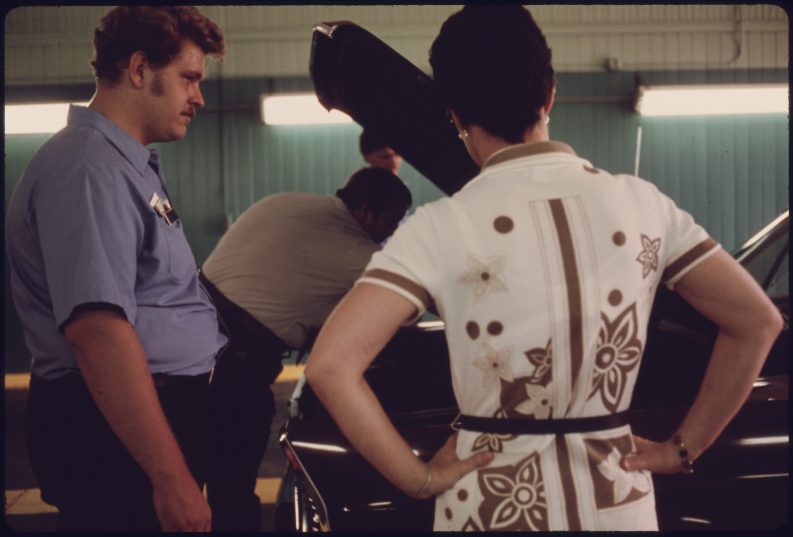 Unhappy Car Owner, Foreground, Watches as Public Works Department Employees Try to Locate the Reason Her Vehicle Failed Its Inspection for the Second Time at an Auto Emission Inspection Station at Norwood, Ohio...08/1975