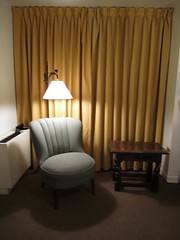A corner of a room with a chair, light, and table, intended as a reading nook.
