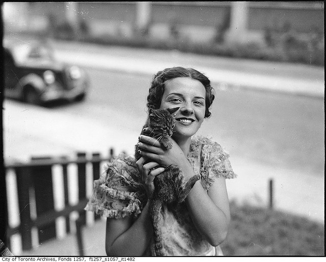 Billie Hallam, Miss Toronto 1937, posing with a kitten, in front yard of her home, 191 Booth Avenue
