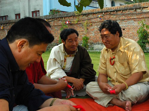 Tibetan men share a story, holding ceremonial red blindfolds, sitting on the lawn, Sakya Lamdre, Tharlam Monastery of Tibetan Buddhism, Boudha, Kathmandu, Nepal by Wonderlane