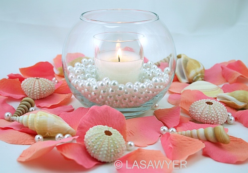 This beachthemed table centerpiece uses silk rose petals in coral 