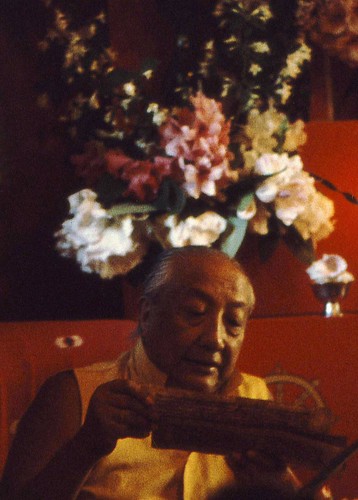 HH Dilgo Khyentse Rinpoche reading a pecha, giving an initiation, with a bouquet of flowers on the shrine behind him, Sakya Ward St Dharma Center, Seattle, Washington, USA 1976 by Wonderlane