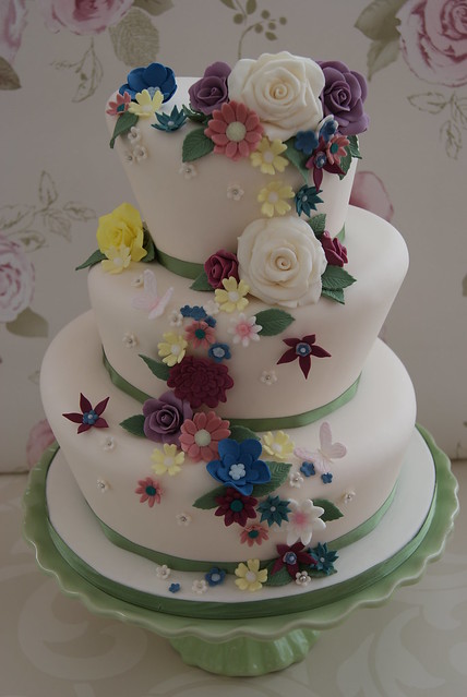 A wonky three tiered wedding cake with a colourful cascade of summer flowers