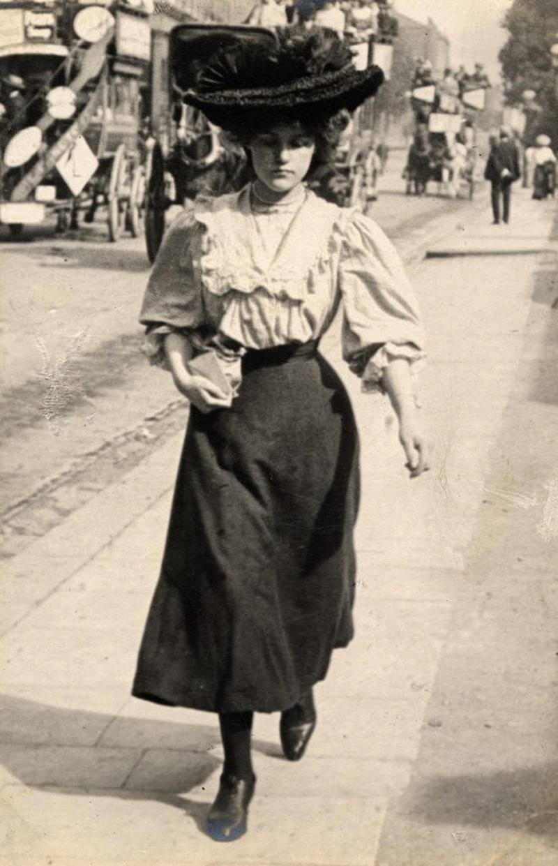 A young woman on Kensington High Street with horse-drawn buses in the background