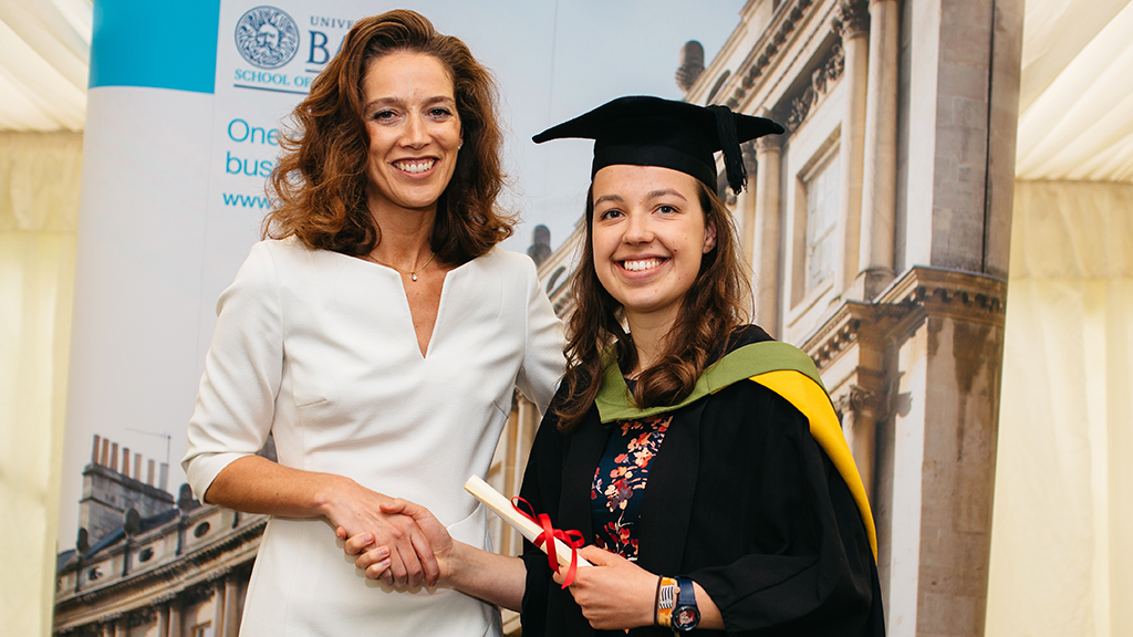 Madelaine Pitt in her graduation gown shaking hands with a woman and holding her degree certificate
