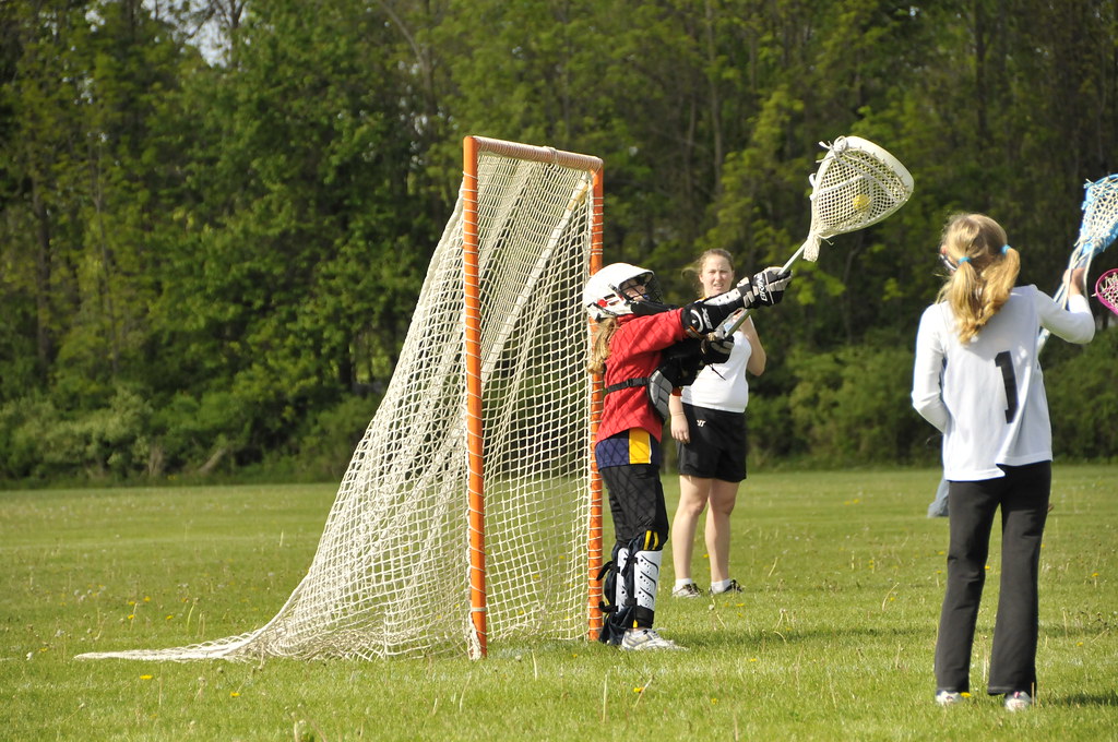 Three young lacrosse players on the field in front of the goal.