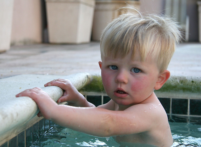 A cautious boy clings to the edge of a swimming pool
