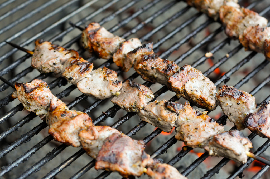 Skewers of meat are cooking over black grills
