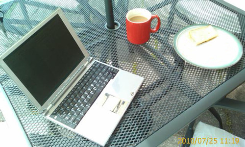 Laptop and working lunch. An outside table with a silver laptop, coffee and a sandwich on it.