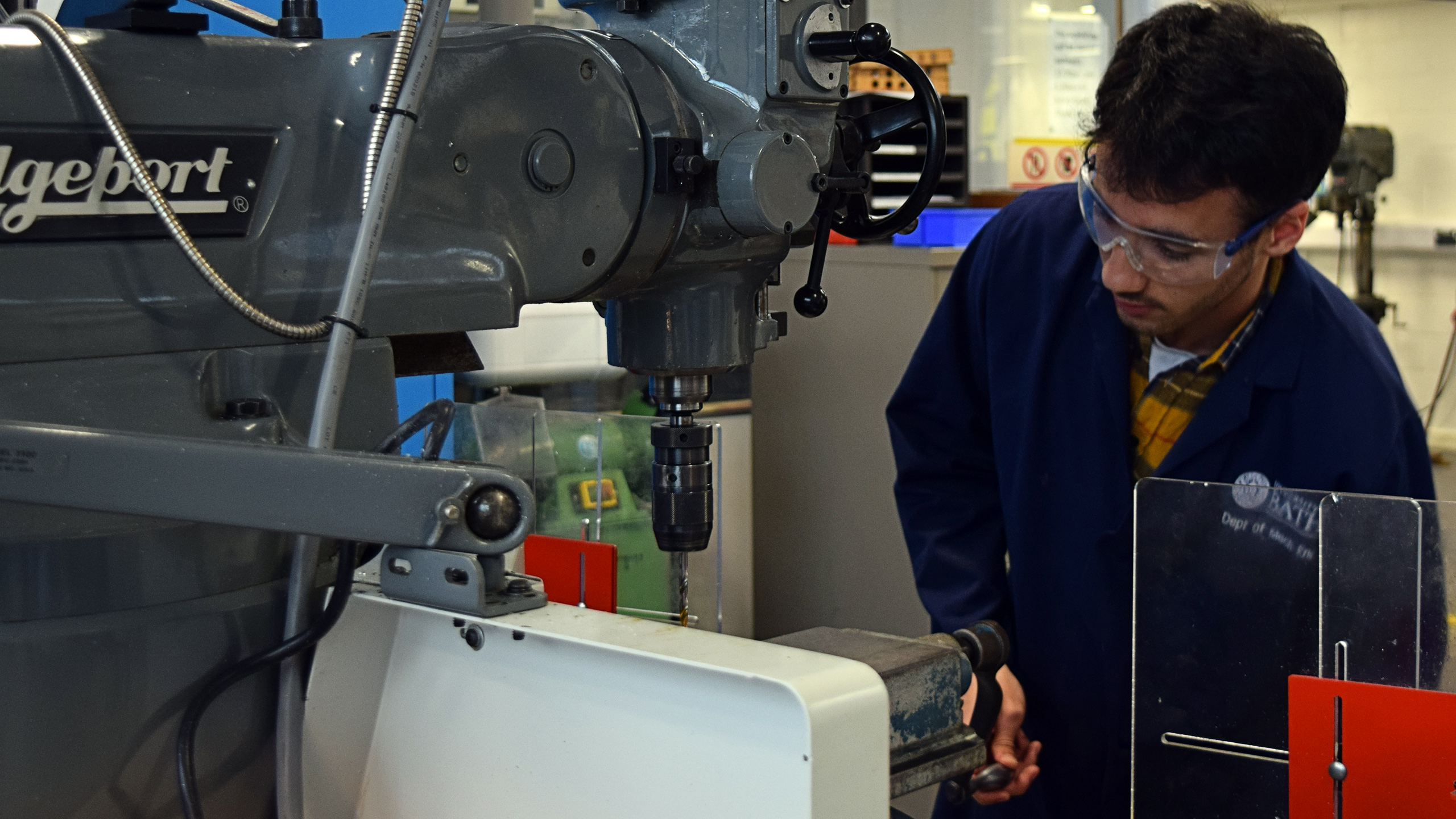 Student in lab coat and goggles works on CNC milling machine in workshop