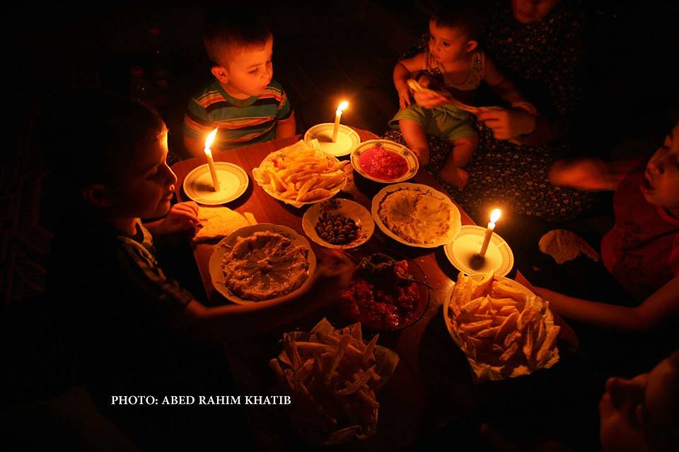 A Palestinian family eats dinner by candlelight at their makeshift home in the Rafah refugee camp, in the southern Gaza