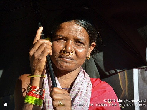 photo physiognomy psychological primelens street portrait closeup sunshine cultural character nose nosepiercing bareheaded bodylanguage gesture consent fun travel market female posing authentic tribal umbrella bothhands bangles color eyes adivasi matthahnewaldphotography face facingtheworld sunlight horizontal head india jeypore woman mature nikond3100 nosejewelry orissa outdoor nosering 50mm oneperson expression halflength earring nikkorafs50mmf18g fullfaceview 4x3ratio 1200x900pixels resized lookingatcamera