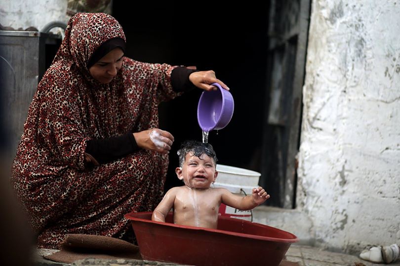 A Palestinian mother showering her baby in a bowl during a heatwave in Gaza City