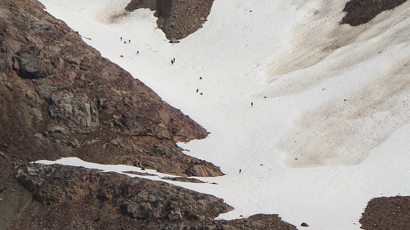 Zoomed-in view of a large group of people descending the snow toward Lyman Lake from Spider Gap