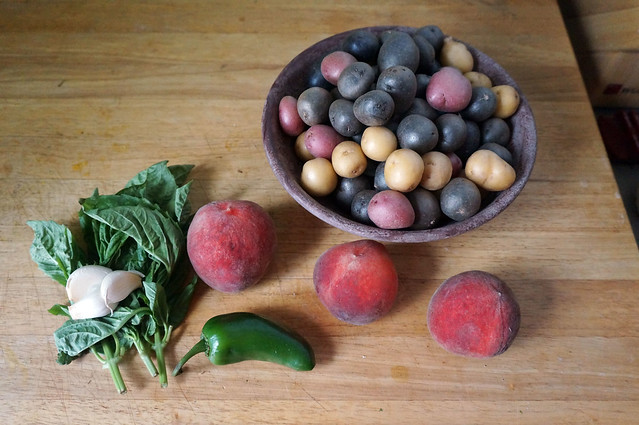 Humble beginnings: a bowl of little potatoes, a small pile of basil and garlic cloves with a jalapeño, and a trio of small, red-cheeked peaches