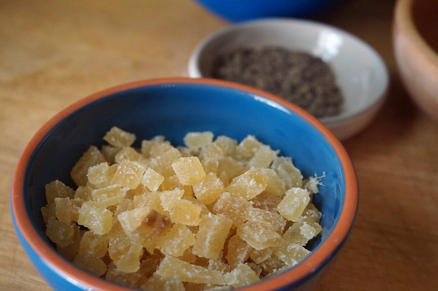 Closeup on a small bowl filled with small squarish chunks of crystallized ginger, the sparkly sugar coating contrasting with the smooth cut edges.