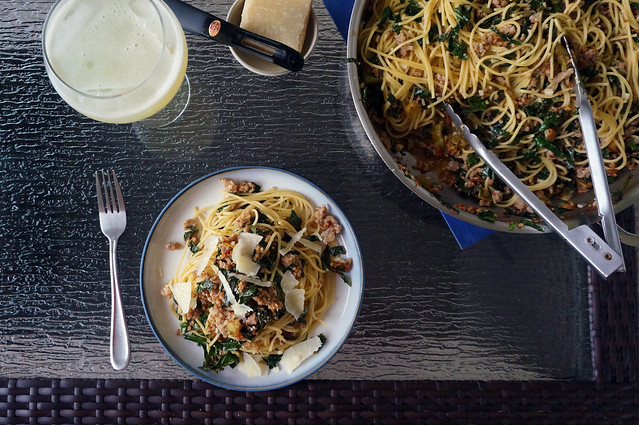 Overhead view of the table, with a plate of spaghetti, a pan of noodles, a tiny plate with Parmesan cheese and a peeler, and a wine goblet filled with fizzy lemonade