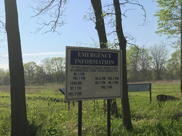Sign showing "Emergency information: If you hear a steady siren for 3-5 minutes, tune your radio to:" with a list of radio stations