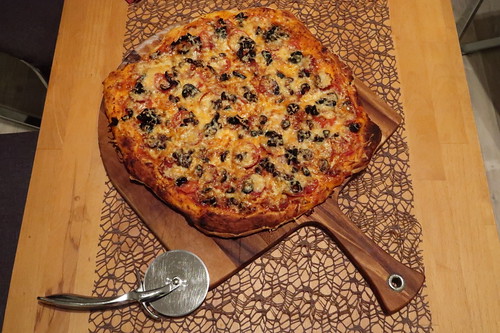 Pizza mit scharfer Salami, schwarzen Oliven und frischen Tomaten