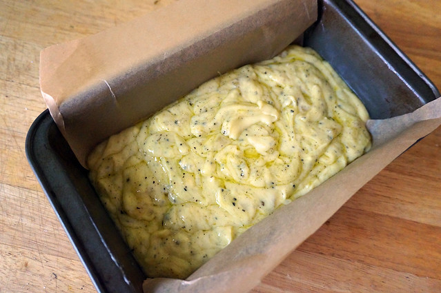 A loaf pan filled with cake batter. The olive oil is mostly incorporated, but stands out in little rivulets between dollops of batter. It looks almost like a loaf of scrambled eggs.
