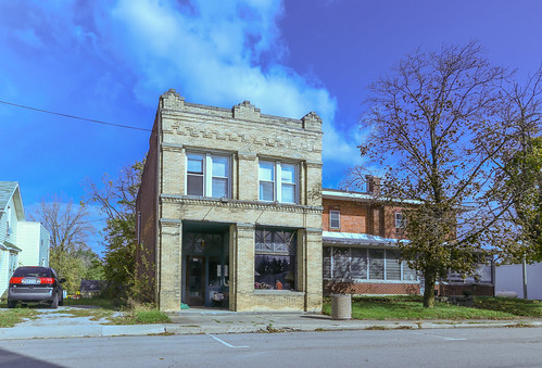 building structure commercial historic ney ohio defiance county twostory 11 windows corbelling corbelled key buff pilasters capitals paired parapet sidewalk street bushes trees sky blue cables wires shadow car vehicle