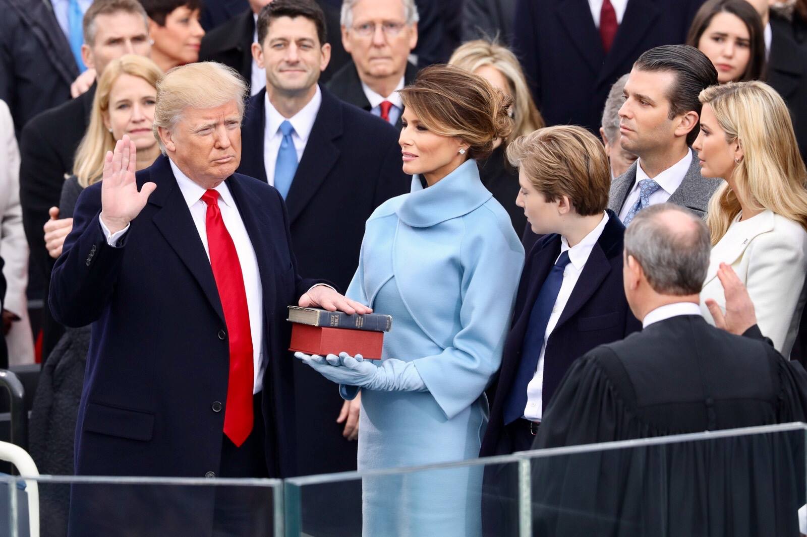 President Donald Trump being sworn in on January 20, 2017 at the U.S. Capitol building in Washington, D.C. Melania Trump wears a sky-blue cashmere Ralph Lauren ensemble. He holds his left hand on two versions of the Bible, one childhood Bible given to him by his mother, along with Abraham Lincoln’s Bible. 