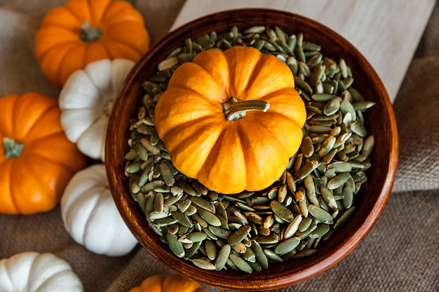 Closeup of Full Bowl of Peeled Pumpkin Seeds with Orange Pumpkin, Autumn Holidays