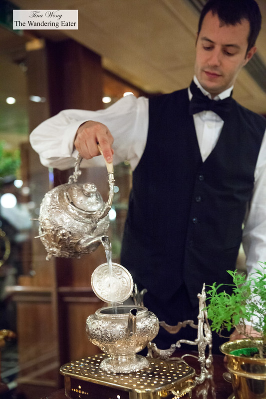 Waiter making the thyme tisane, pouring hot water into the ornate silver teapot