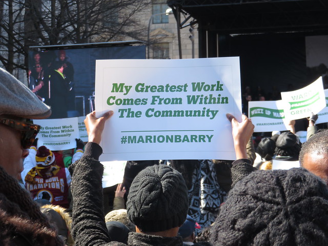 A crowd member holds up a sign with a quote from Marion Barry: 