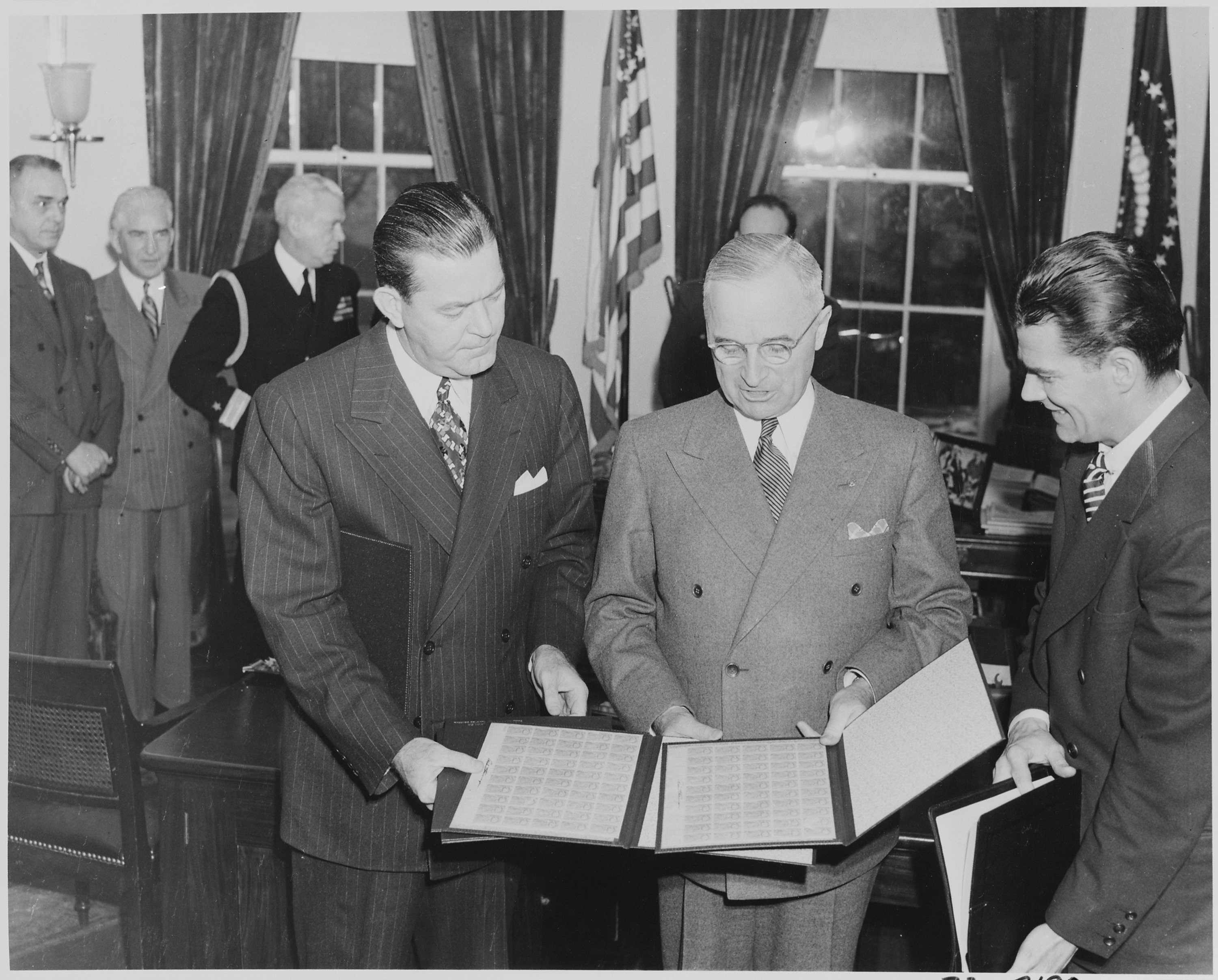 President Harry S. Truman receiving a set of stamps honoring the late President Franklin D. Roosevelt from Postmaster General Robert Hannegan (to the President's right), January 30, 1946.
