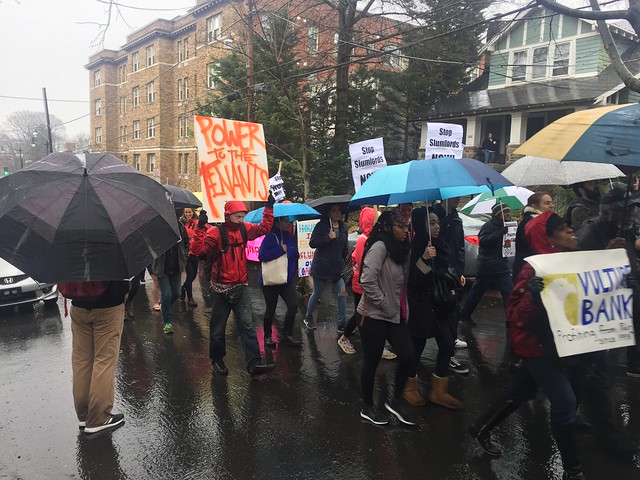Protesters marching down a street holding umbrellas.