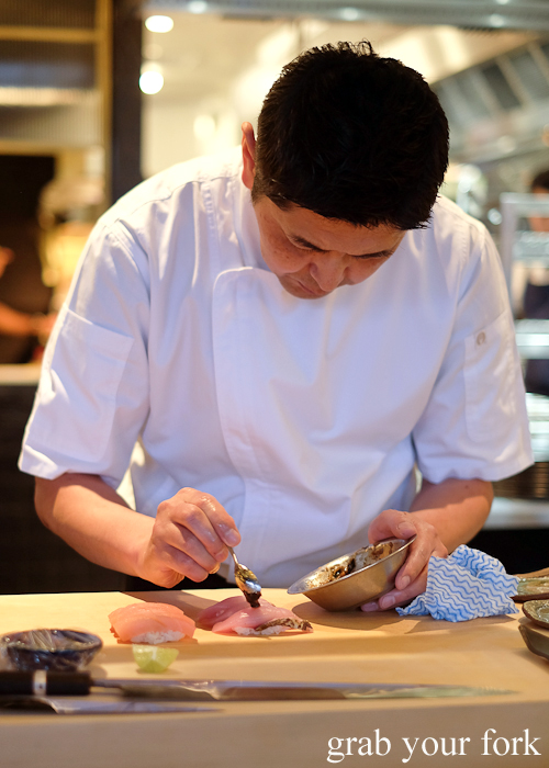 Chef Ryuichi Yoshii spooning ume and nori glaze onto bonito sushi at Fujisaki by Lotus at Barangaroo in Sydney