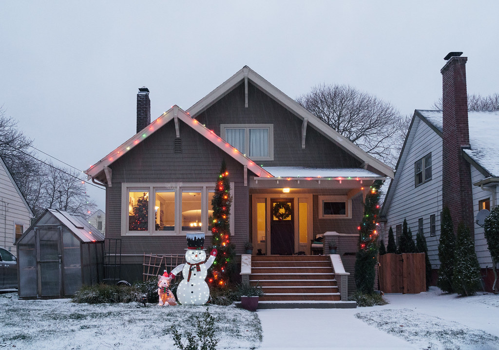 Snow falls at a house decorated with Christmas lights including a dog and snowman