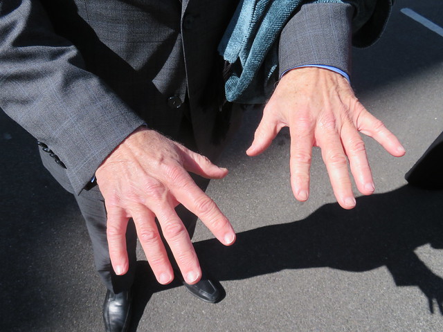Photo of a man in a dark suit holding out his two hands. His shadow stretches off to the right.