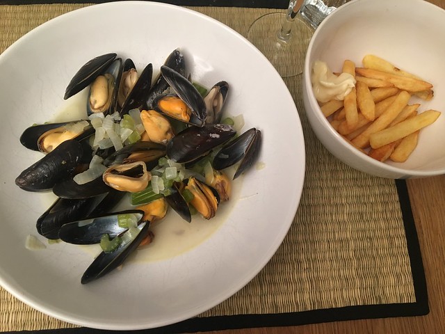 A large bowl of mussels in sauce with a small bowl of chips next to it.