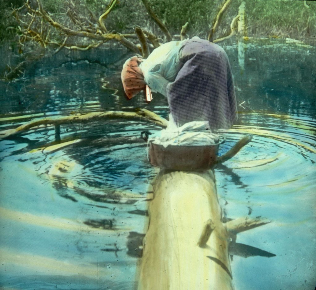 Крестьянка стоит на упавшем бревне над ручьем и стирает белье